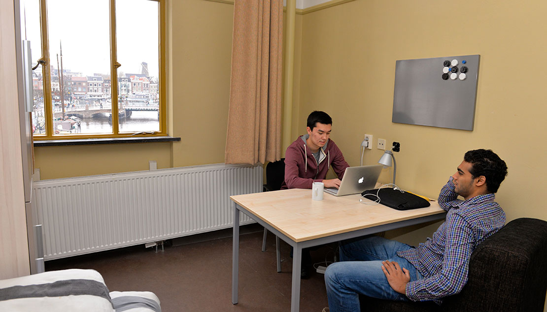 Two students sitting at a table talking in dorm. 