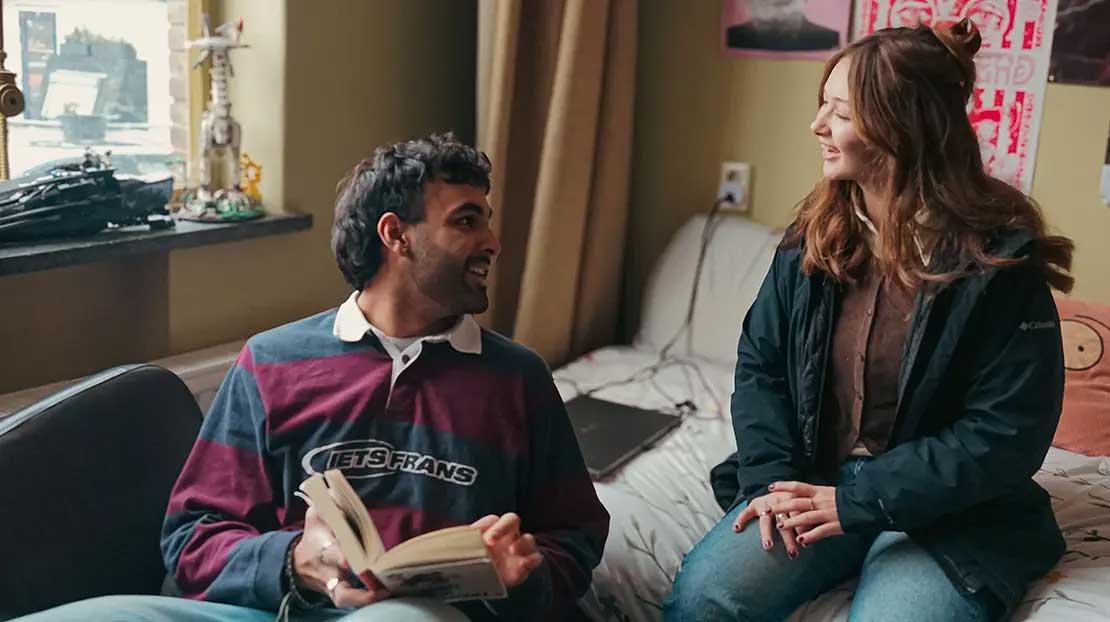 Two students sitting in a dorm room talking and laughing.