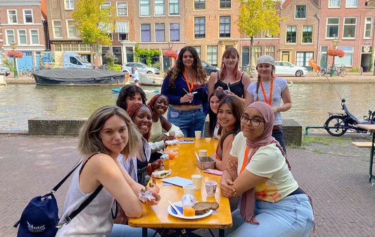 New Webster Leiden students smiling and eating lunch by the canal during orientation.